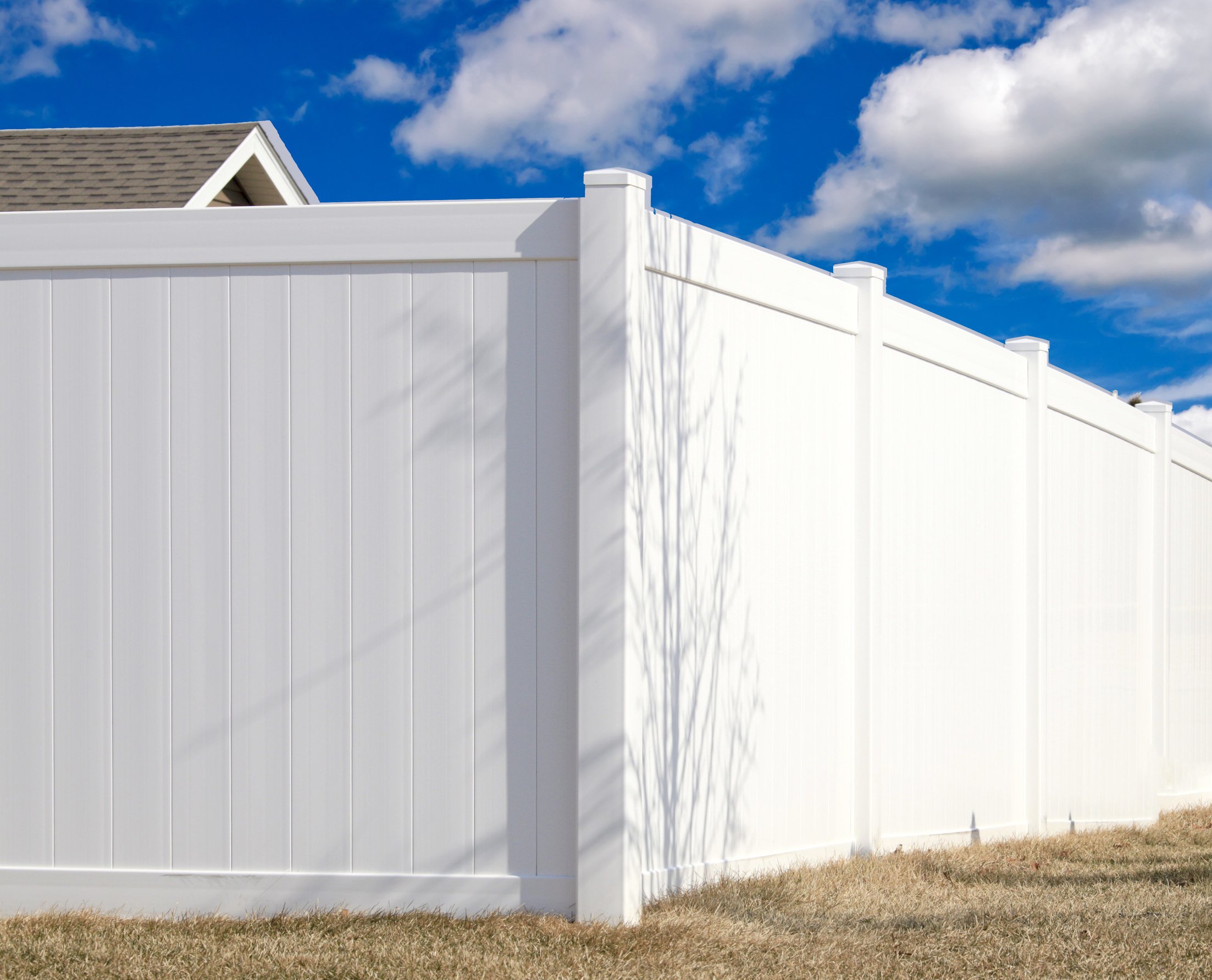 angled white vinyl fencing in a yard. Blue sky and clouds are in the background